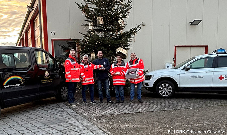 Benjamin Dittus vom ambulanten Pflegedienst Lichtblick und Vertreter des DRK-Ortsvereins Calw stehen zusammen bei der Übergabe der vorbereiteten Weihnachtsgrüße. Beide lächeln in die Kamera. Die kleinen Präsente sind sichtbar und werden symbolisch überreicht.