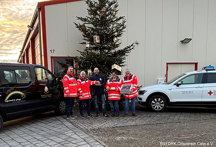 Übergabe an den ambulanten Pflegedienst Lichtblick Benjamin Dittus vom ambulanten Pflegedienst Lichtblick und Vertreter des DRK-Ortsvereins Calw stehen zusammen bei der Übergabe der vorbereiteten Weihnachtsgrüße. Beide lächeln in die Kamera. Die kleinen Präsente sind sichtbar und werden symbolisch überreicht.